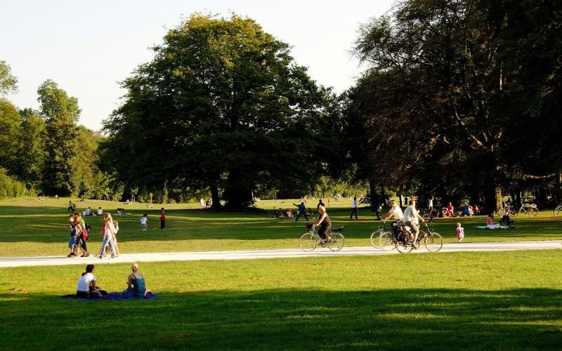 A park with many people riding bikes, having a picnic, and walking.