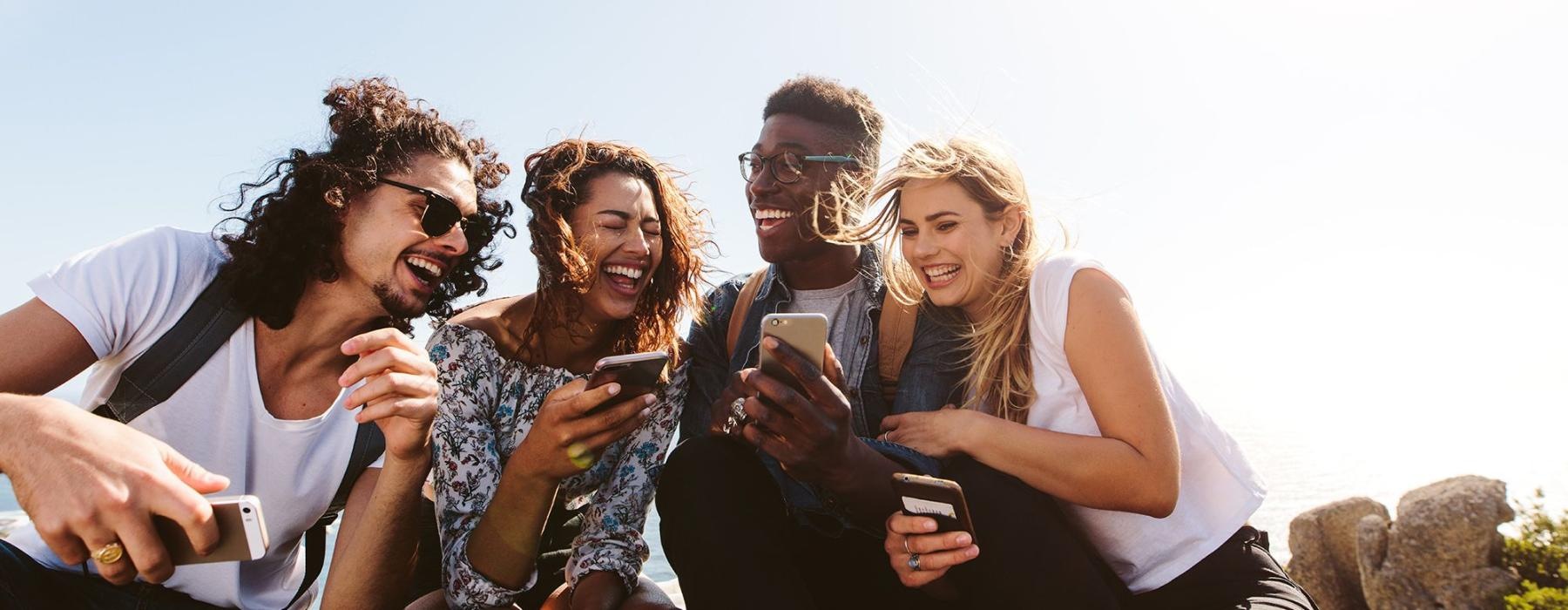 a group of friends sit outside laughing over their cell phones